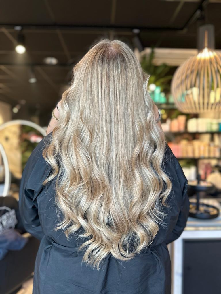 De achterkant van een vrouw die haar lange blonde haar blondeert in een salon.