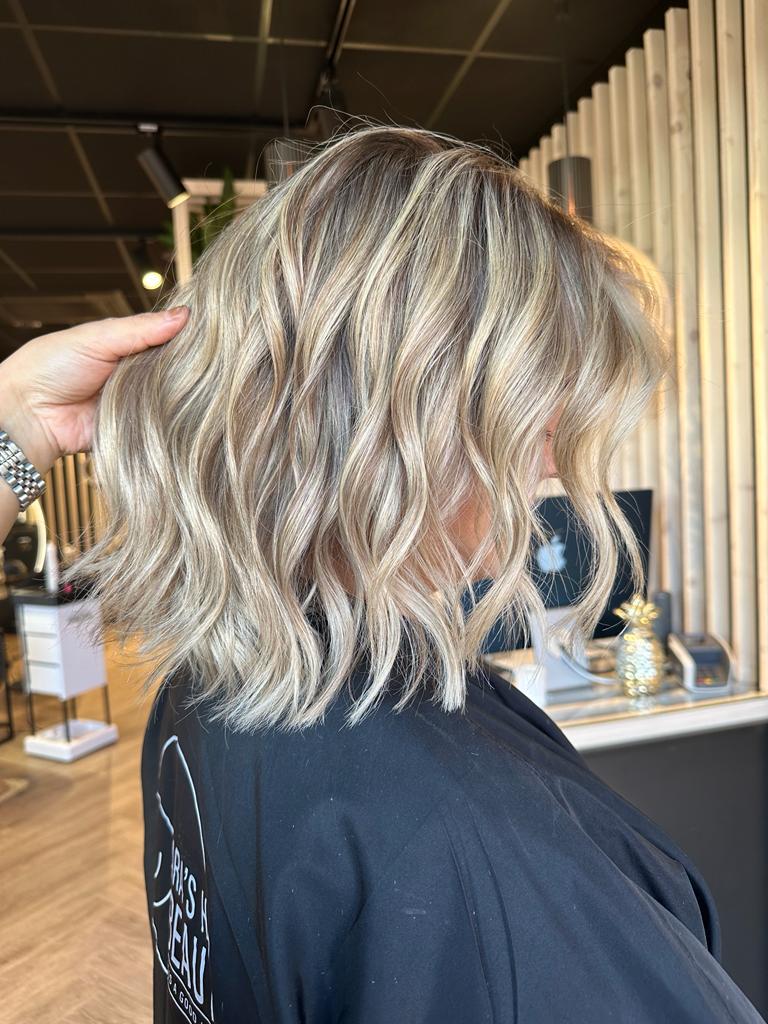 Een haarstylist die een blondeerbehandeling uitvoert op de achterkant van het haar van een vrouw in een salon.